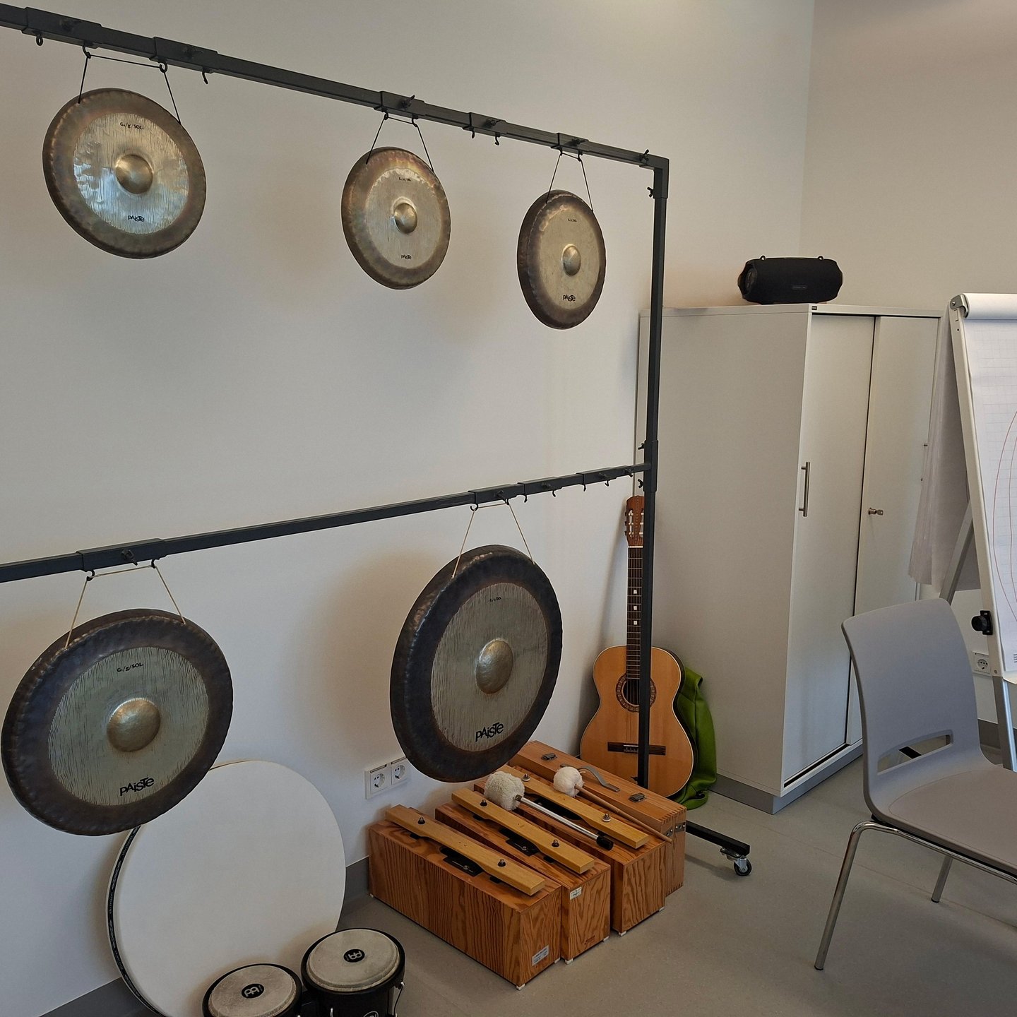 Raum mit mehreren aufgehängten Gongs, weiteren Klanginstrumenten, Gitarre, Schrank und Flipchart.