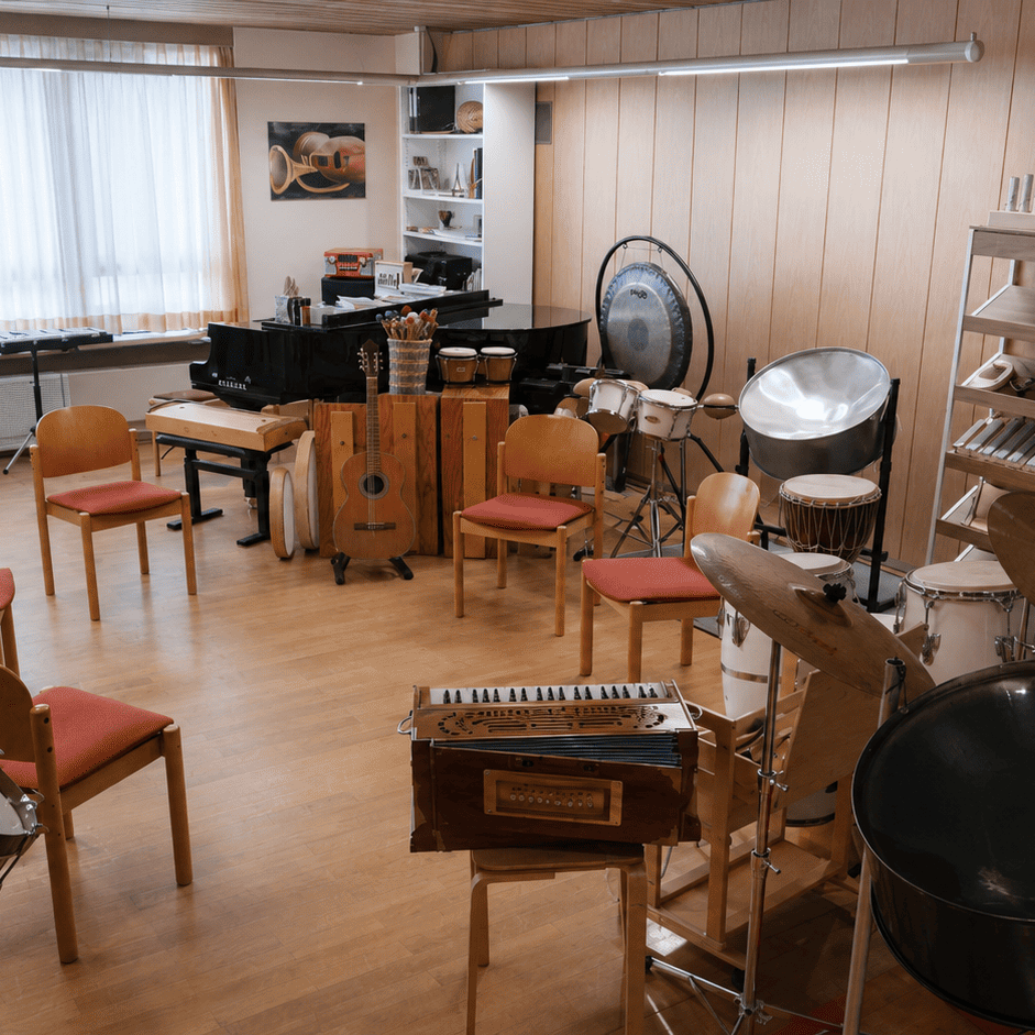 Musikraum mit vielen Instrumenten (Klavier, Gitarre, Trommel,...) und einem Stuhlkreis